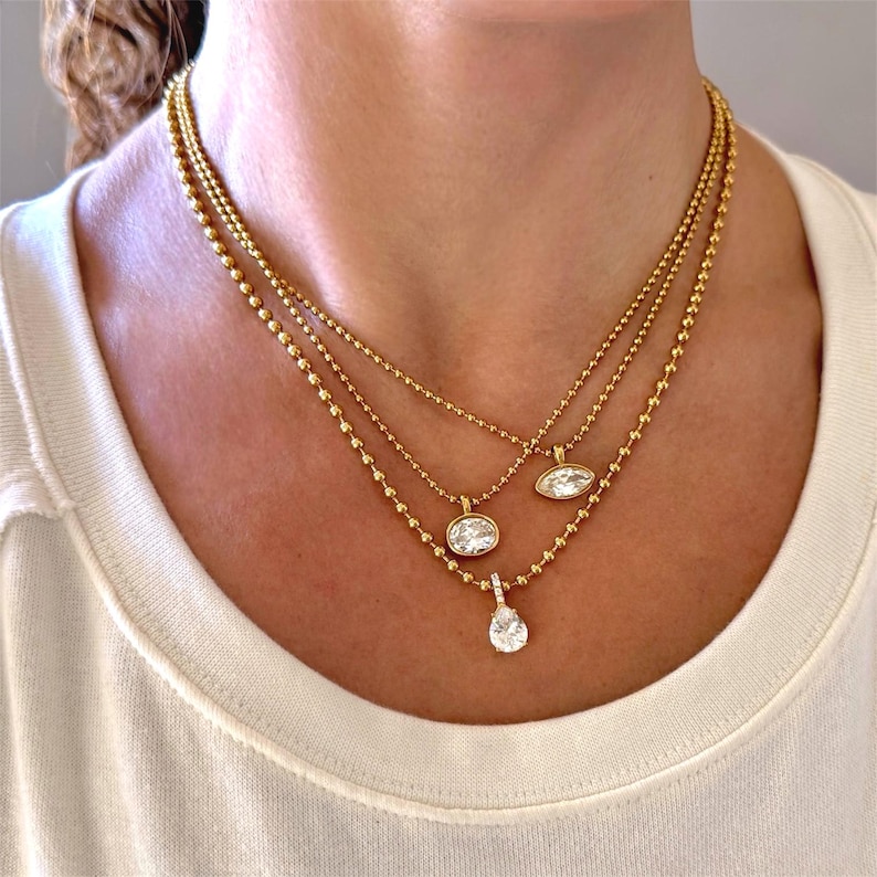 Three 18K PVD gold ball chain CZ pendant necklaces layered on neck showing marquise, oval and pear cubic zirconia styles adjustable from 16 to 18 inches