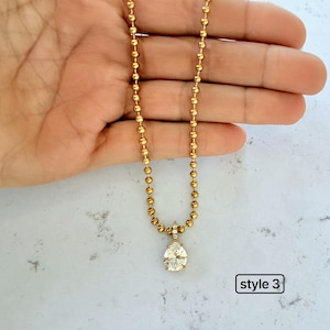 Pear shaped cubic zirconia pendant on 18K PVD gold 3mm ball chain held in palm showing teardrop CZ with pavé set bail on bold gold ball chain, style 3