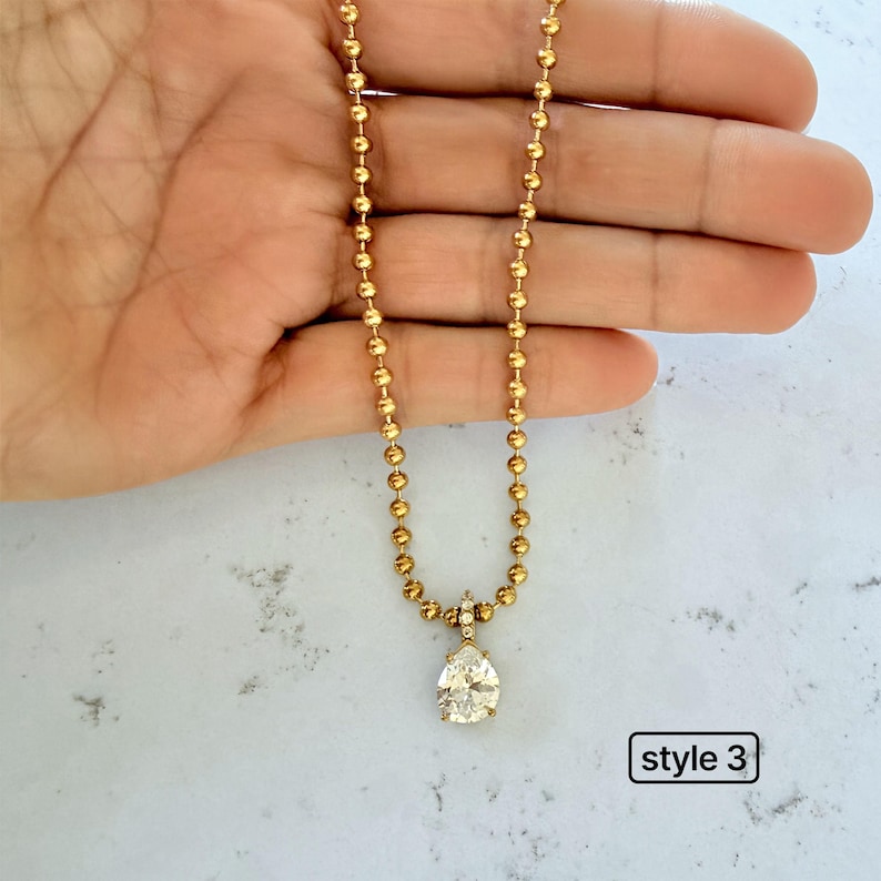 Pear shaped cubic zirconia pendant on 18K PVD gold 3mm ball chain held in palm showing teardrop CZ with pavé set bail on bold gold ball chain, style 3