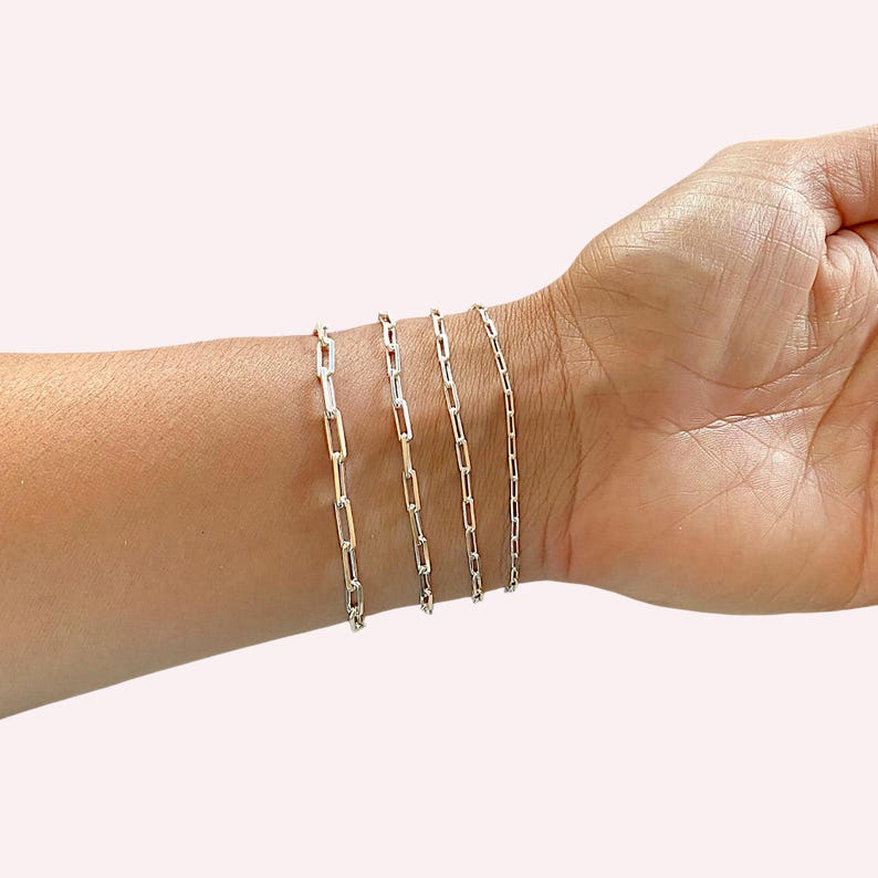 May include: Five silver chain bracelets of varying lengths and widths, shown on a person's wrist.