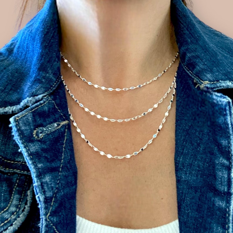 May include: A layered silver necklace with a delicate chain featuring small oval-shaped links.