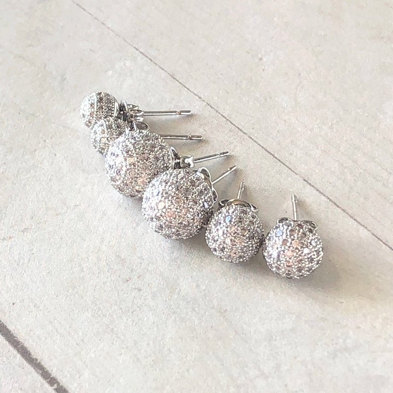 Five round pave silver stud earrings with sparkly, cubic zirconia stones, shown in 6mm, 8mm and 10mm. The earrings are arranged in order of size, with the largest earring on the left and the smallest earring on the right.