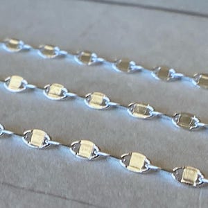 May include: Three silver chains with a delicate, oval-shaped link design. The chains are arranged in a row, with the top chain being the longest and the bottom chain being the shortest.