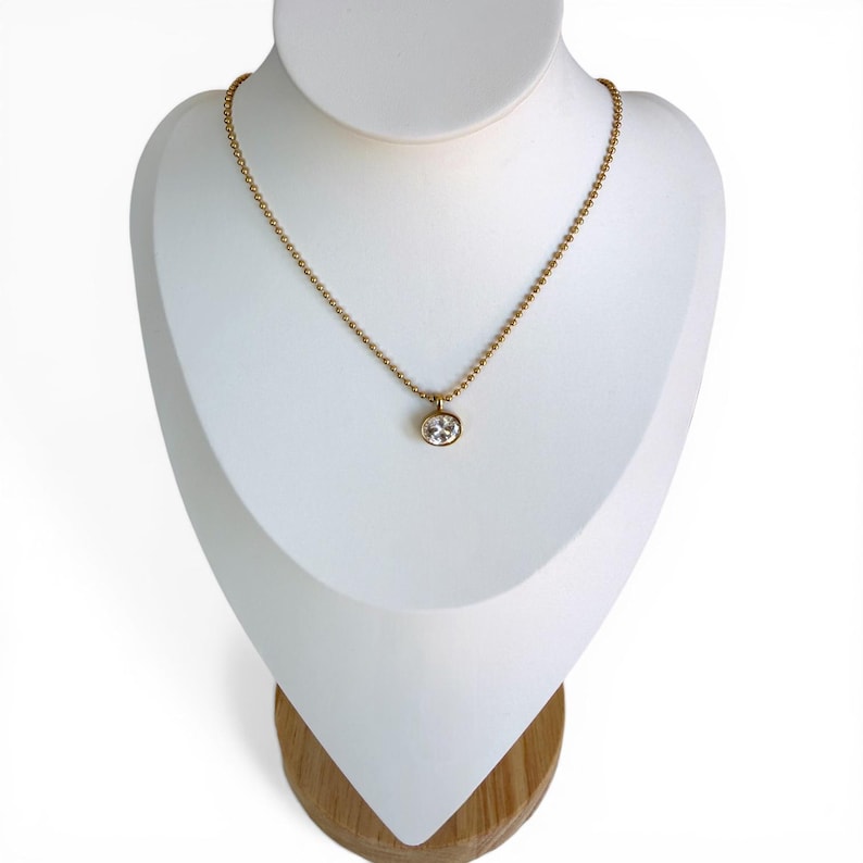 Oval cubic zirconia pendant necklace on white jewelry bust showing 18K PVD gold 2mm ball chain with bezel set CZ pendant, style 2