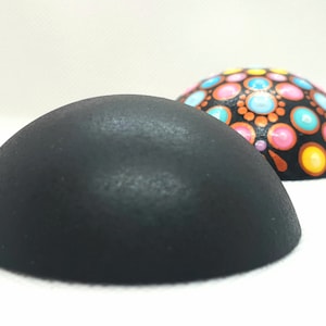 Può includere: Due oggetti decorativi a forma di mezza sfera. L'oggetto in primo piano è nero pieno. L'oggetto sullo sfondo è decorato con un motivo a pois colorati in rosa, blu, giallo e arancione su sfondo nero. Entrambi gli oggetti sono su una superficie bianca.
