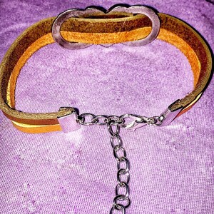 May include: A layered leather bracelet with a silver-tone clasp and chain extender. The bracelet features three bands of leather in shades of brown and yellow. The bracelet has a decorative silver-tone clasp.