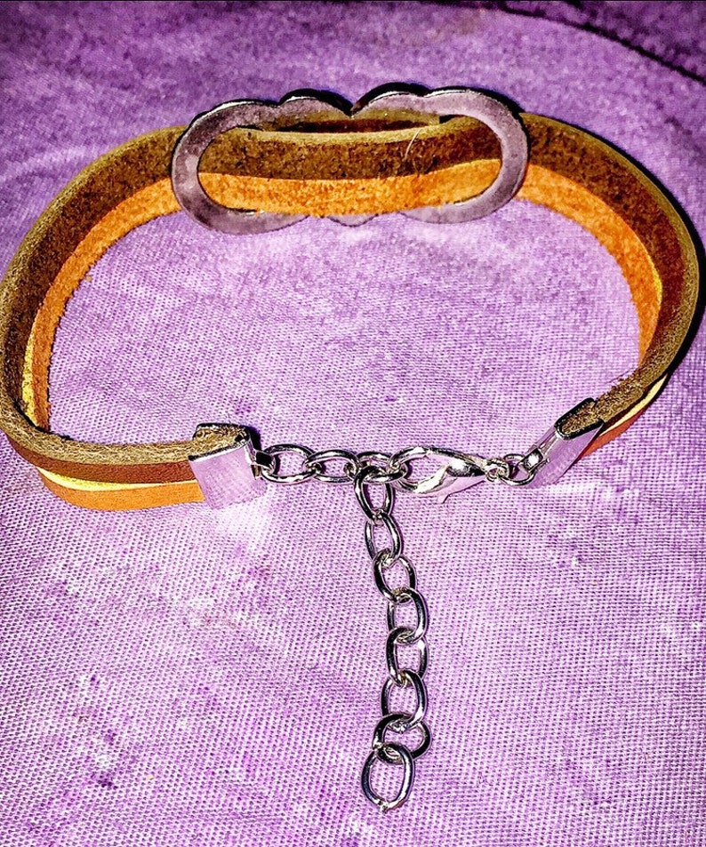 May include: A layered leather bracelet with a silver-tone clasp and chain extender. The bracelet features three bands of leather in shades of brown and yellow. The bracelet has a decorative silver-tone clasp.