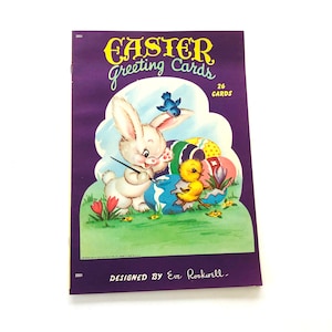 May include: A vintage book of 26 Easter greeting cards featuring a white bunny painting an egg with a bluebird and two yellow chicks. The book cover is purple with the text "Easter Greeting Cards" and "Designed by Eve Rockwell".