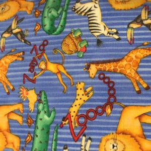 May include: A blue and white striped fabric with a repeating pattern of various animals, including giraffes, zebras, lions, monkeys, and crocodiles. The fabric has the words "Zany Zoo" printed on it.