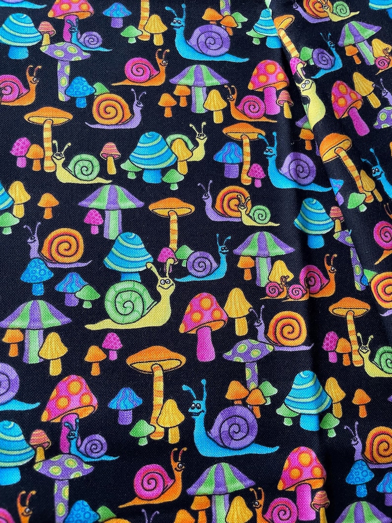 Op de afbeelding: Een zwarte stof met een herhalend patroon van kleurrijke slakken en paddenstoelen. De slakken zijn in verschillende kleuren, waaronder blauw, groen, geel en roze. De paddenstoelen zijn ook in verschillende kleuren, waaronder rood, oranje, geel en paars.