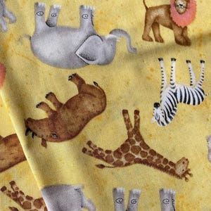 May include: Yellow fabric with a repeating pattern of safari animals. The design includes giraffes, zebras, lions, and hippos. The animals are in various poses, with a watercolor style.