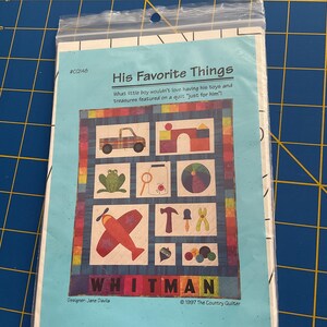 May include: A quilt pattern titled "His Favorite Things" featuring colorful illustrations of a truck, frog, airplane, and tools. The pattern is designed by Jane Davila and published by The Country Quilter.