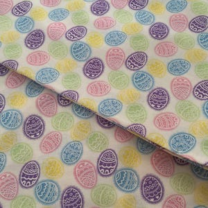 May include: A fabric with a repeating pattern of pastel-colored Easter eggs. The eggs are in shades of pink, blue, yellow, green, and purple, each with a white decorative design. The fabric has a white background.