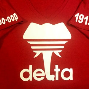 May include: Red t-shirt with a white elephant graphic and the word "delta" underneath. The sleeves have the text "00-000" and "1913" printed on them.