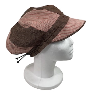 May include: A brown and pink striped newsboy cap with a short brim. The cap is made of a textured fabric and features a drawstring adjustment at the back. The hat is displayed on a white mannequin head.