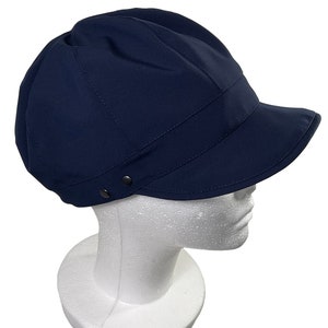 Könnte beinhalten: Eine marineblaue,  Baumwoll-Newsboy-Kappe mit flachem Schirm. Die Kappe hat eine leicht abgerundete Krone und einen Knopf oben.