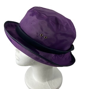May include: A purple rain hat with a black band and two gold eyelets. The hat has a wide brim and is made of a water-resistant material.