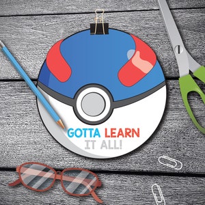 May include: A red, white, and blue Pokeball with the text "Gotta Learn It All!" printed on it. The Pokeball is attached to a wooden surface with a silver paper clip.