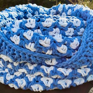 May include: A handmade, blue and white crocheted cowl scarf. The scarf is made of a soft, plush yarn, with a repeating pattern of white and blue sections. The cowl is circular and appears to be warm and cozy.