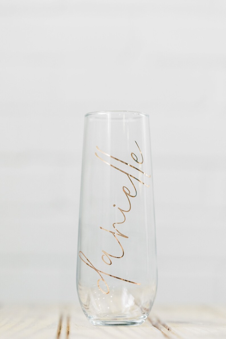 May include: A clear glass champagne flute with the word "Brielle" written in gold lettering.