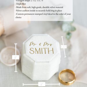 May include: An off-white, octagon-shaped velvet ring box featuring a triple slot interior. The lid is customized with gold text reading Mr & Mrs SMITH. The box measures 2 inches by 2 inches by 1.75 inches as indicated by the visible dimension lines.
