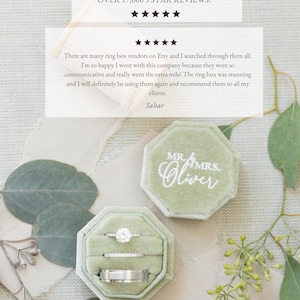 May include: An octagonal sage green velvet ring box with a lid featuring the white embroidered text MR. & MRS. Oliver. The open box contains three silver-toned rings, including one with a large round stone and two plain bands, displayed in slots.