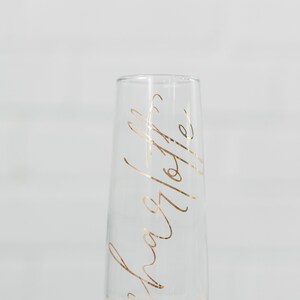 May include: A clear glass champagne flute with a gold inscription that reads "Cheers to the happy couple".