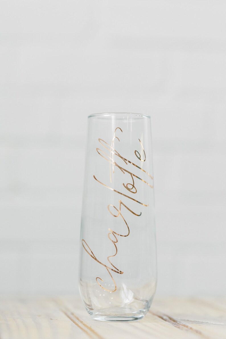 May include: A clear glass champagne flute with a gold inscription that reads "Cheers to the happy couple".
