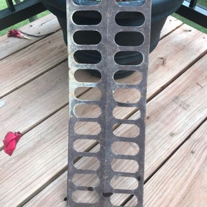 May include: A rusty metal grate with 14 oval-shaped holes. The grate is rectangular and has a slightly curved edge.