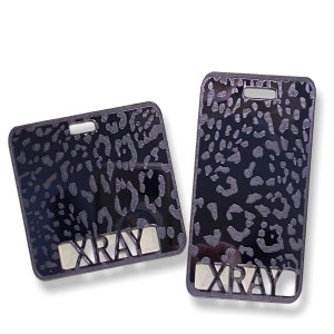 May include: Two black and silver keychains with a leopard print design. The keychains have the word "XRAY" cut out of the metal.