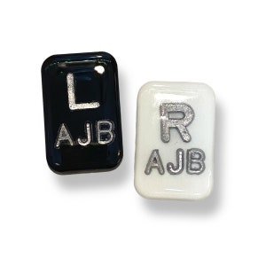 May include: Two rectangular, glossy tiles. One is black with a silver "L" and "AJB" text. The other is white with a silver "R" and "AJB" text. The tiles are likely for a craft or decorative project.