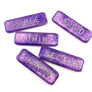 May include: Five rectangular purple glitter labels with silver lettering. The labels read: PUREE, SOLID, THIN, HONEY, and NECTAR. The labels are arranged on a white background.