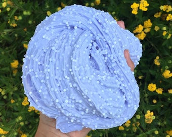 May include: A large clump of light purple slime with white beads throughout. The slime is being held in a hand.