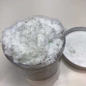 May include: A clear plastic jar filled with white bath salts. The salts are fluffy and have a slightly green tint.