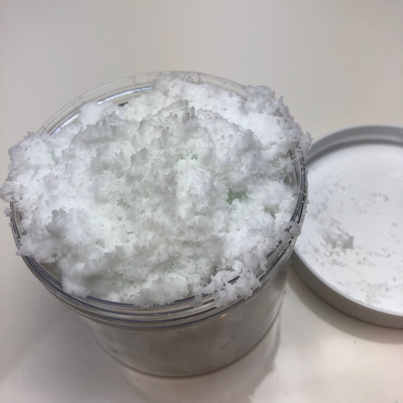 May include: A clear plastic jar filled with white bath salts. The salts are fluffy and have a slightly green tint.