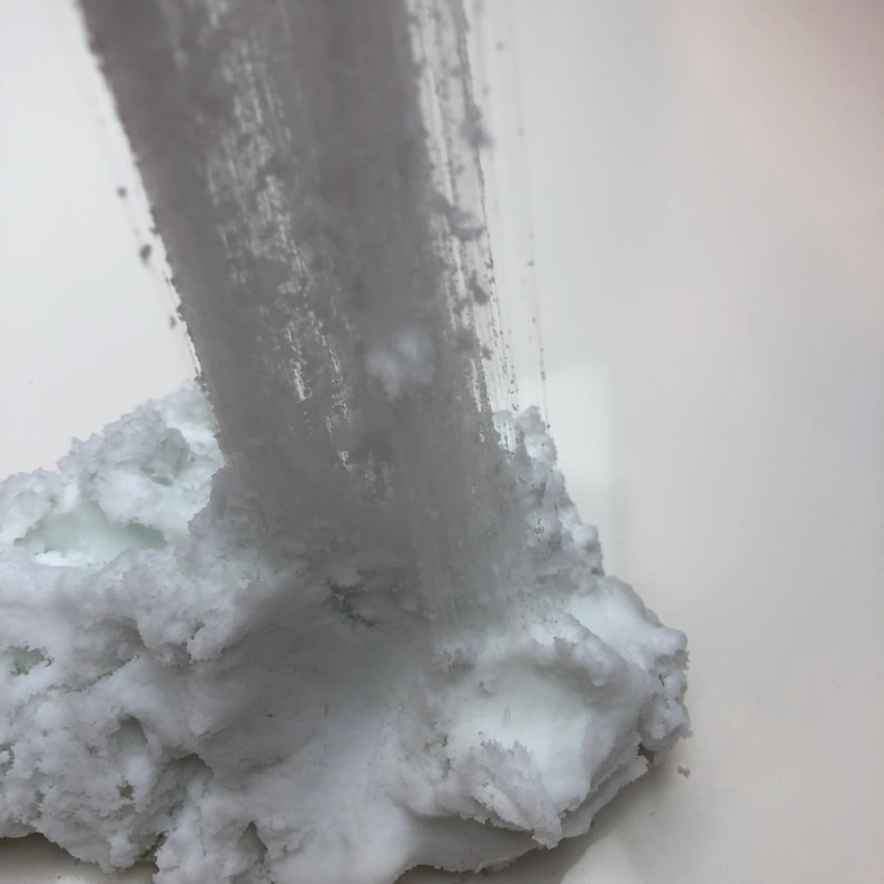 May include: White slime being pulled from a large pile of white slime. The slime has a grainy texture.