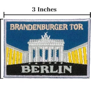 Könnte beinhalten: Gestickter Aufnäher mit dem Brandenburger Tor in Berlin. Der Aufnäher ist rechteckig und misst 7,6 cm breit und 5,1 cm hoch. Das Design enthält den Text "BRANDENBURGER TOR" und "BERLIN" auf blauem Hintergrund.