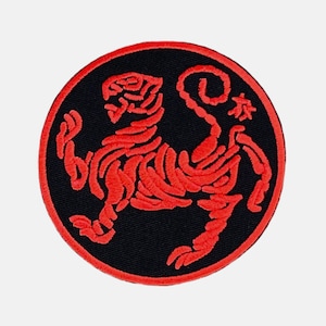 Può includere: Toppa di arti marziali ricamata in rosso con sfondo nero. La toppa presenta una tigre rossa stilizzata con il carattere giapponese per "legno" nell'angolo in alto a destra.
