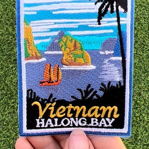 Könnte beinhalten: Gestickter Aufnäher mit einer malerischen Aussicht auf die Halong-Bucht in Vietnam. Der Aufnäher hat einen blauen Rand und zeigt eine tropische Insel mit einer Palme, einem Segelboot und einer felsigen Küste. Der Text "Vietnam HALONG BAY" ist in Weiß und Gelb auf schwarzem Hintergrund gestickt.