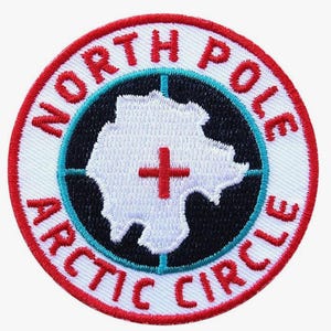 Può includere: Toppa ricamata con le parole "NORTH POLE ARCTIC CIRCLE" in rosso sul bordo. Il centro presenta una mappa bianca con una croce rossa, circondata da un cerchio nero e un anello turchese.