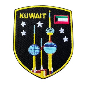May include: A black and yellow embroidered patch with the word "KUWAIT" in yellow lettering. The patch features a depiction of the Kuwait Towers, a flag of Kuwait, and five white stars.