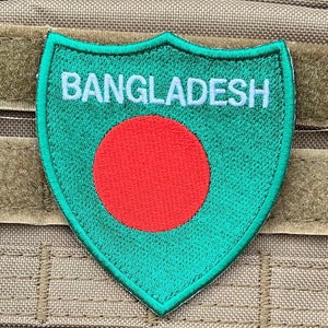 Könnte beinhalten: Ein grüner und roter gestickter Aufnäher mit dem Wort "BANGLADESH" in weißen Buchstaben. Der Aufnäher hat die Form eines Schildes und zeigt einen roten Kreis in der Mitte.