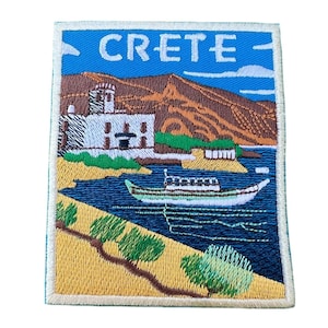 Op de afbeelding: Geborduurde patch met een kleurrijk beeld van een gebouw, een boot en een strand. De tekst "CRETE" is geborduurd in wit op een blauwe achtergrond.