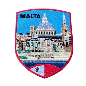 Peut inclure: Un écusson brodé représentant une ville de Malte, avec un ciel bleu et le texte "MALTA" en noir. L'écusson est en forme de bouclier et a une bordure rouge avec une croix maltaise blanche au centre.