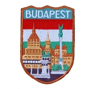 Può includere: Una toppa ricamata con un designo a forma di scudo. La toppa presenta una città di Budapest, Ungheria, con la bandiera ungherese sullo sfondo. Il testo "BUDAPEST" è ricamato in bianco nella parte superiore dello scudo.
