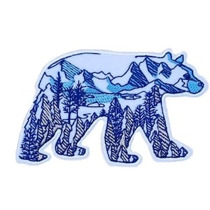 Może przedstawiać: Naszywka haftowana w kolorze niebieskim i białym przedstawiająca niedźwiedzia z górskim krajobrazem w jego sylwetce.