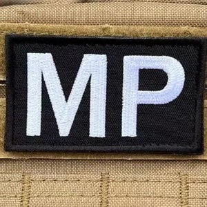 Könnte beinhalten: Schwarzer Patch mit weißen gestickten Buchstaben "MP" auf einem braunen Hintergrund.
