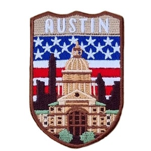 Könnte beinhalten: Gestickter Aufnäher mit dem Wort "AUSTIN" in weißer Schrift auf braunem Hintergrund. Der Aufnäher zeigt ein stilisiertes Bild des Texas State Capitol mit einer amerikanischen Flagge dahinter.