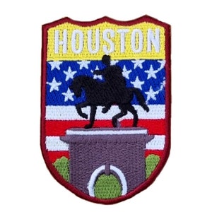 Pode incluir: Um remendo bordado com um fundo de bandeira americana vermelho, branco e azul. O remendo tem a forma de um escudo e tem a palavra "HOUSTON" em letras brancas sobre um fundo amarelo. Uma silhueta preta de uma pessoa a cavalo está na frente da bandeira.