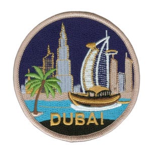 Op de afbeelding: Ronde geborduurde patch met bezienswaardigheden van Dubai, waaronder de Burj Khalifa en Burj Al Arab. De patch heeft een marineblauwe achtergrond, een gouden rand en het woord "DUBAI" in goud.